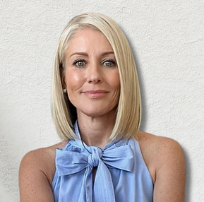 A woman with blond hair wearing a light blue sleeveless top with a bow is smiling against a light-colored background.