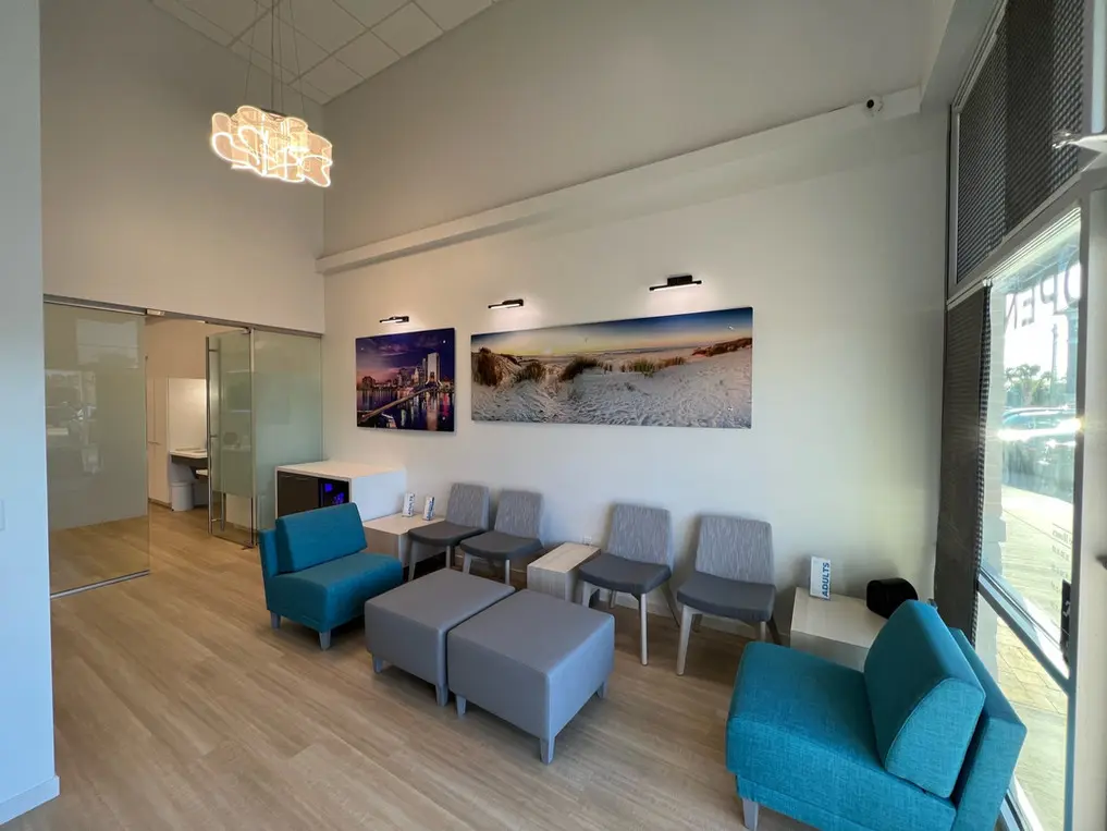 Modern waiting area at Bold Bite Orthodontics in Jacksonville, FL. Features light flooring, gray and teal seating, high ceiling, and large wall art. An inviting and bright orthodontic office space.