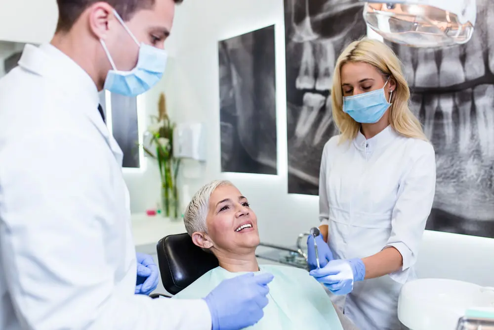 Dentist and assistant with masks prepare dental instruments while adult patient sits in chair smiling at Bold Bite orthodontics.