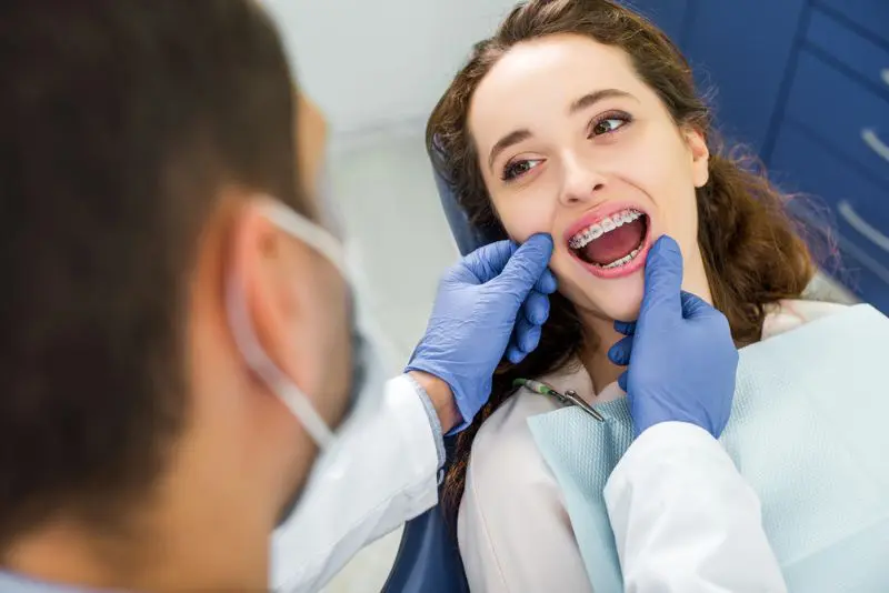 Dentist wearing gloves examines a smiling woman with metal braces in a dental chair in Jacksonville, FL.