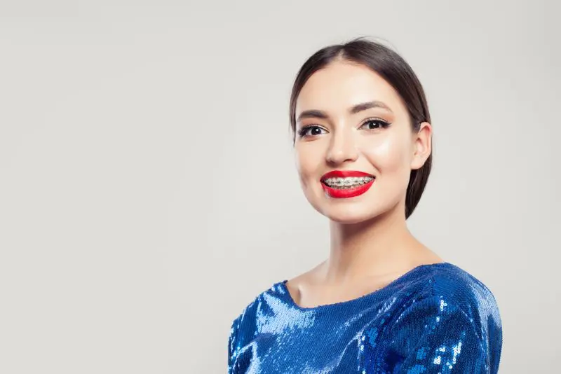 Smiling person with metal braces, wearing a shiny blue top against a plain background in Jacksonville, FL.