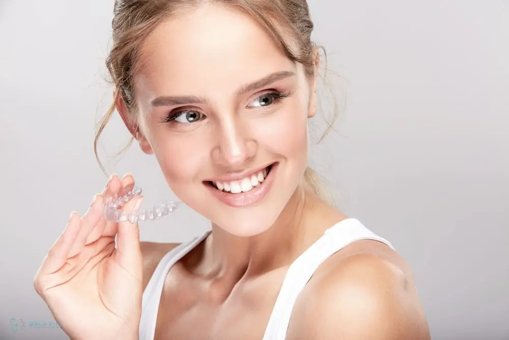 Smiling woman holding an invisalign clear dental aligner near her face as one of the alternatives to braces in Jacksonville, FL against a plain background.