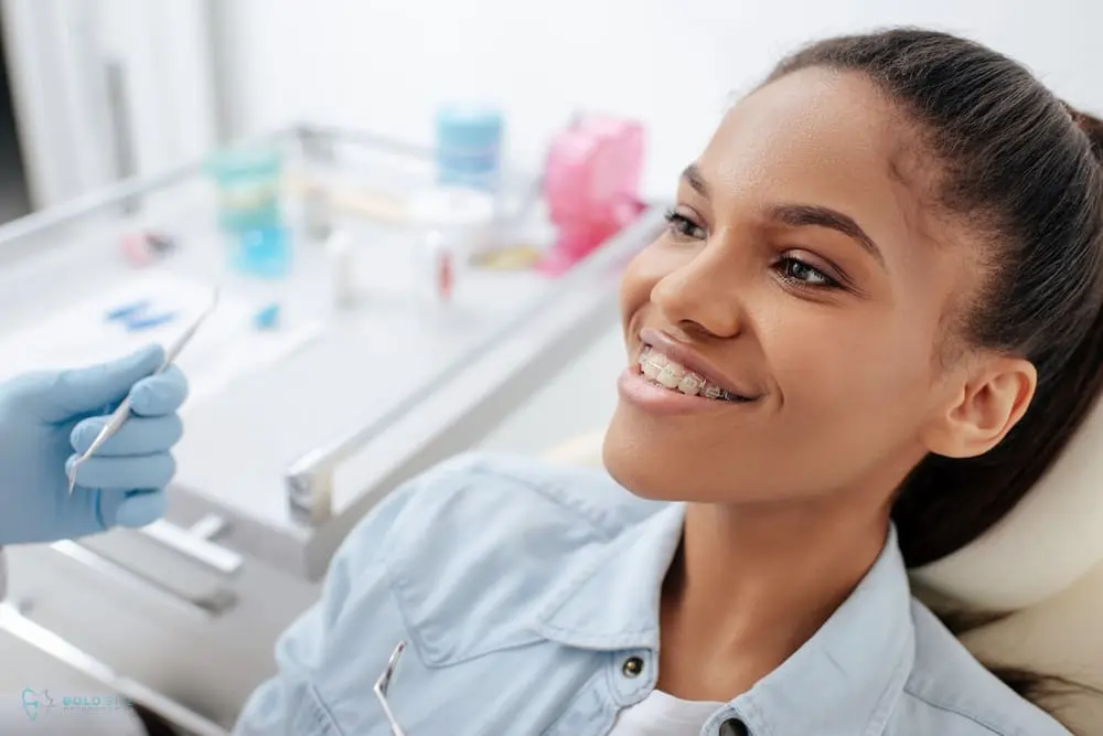 A girl with clear braces as one of the alternatives to braces in Jacksonville, FL sits in a dental chair, smiling while a dentist wearing gloves holds a dental tool near her.