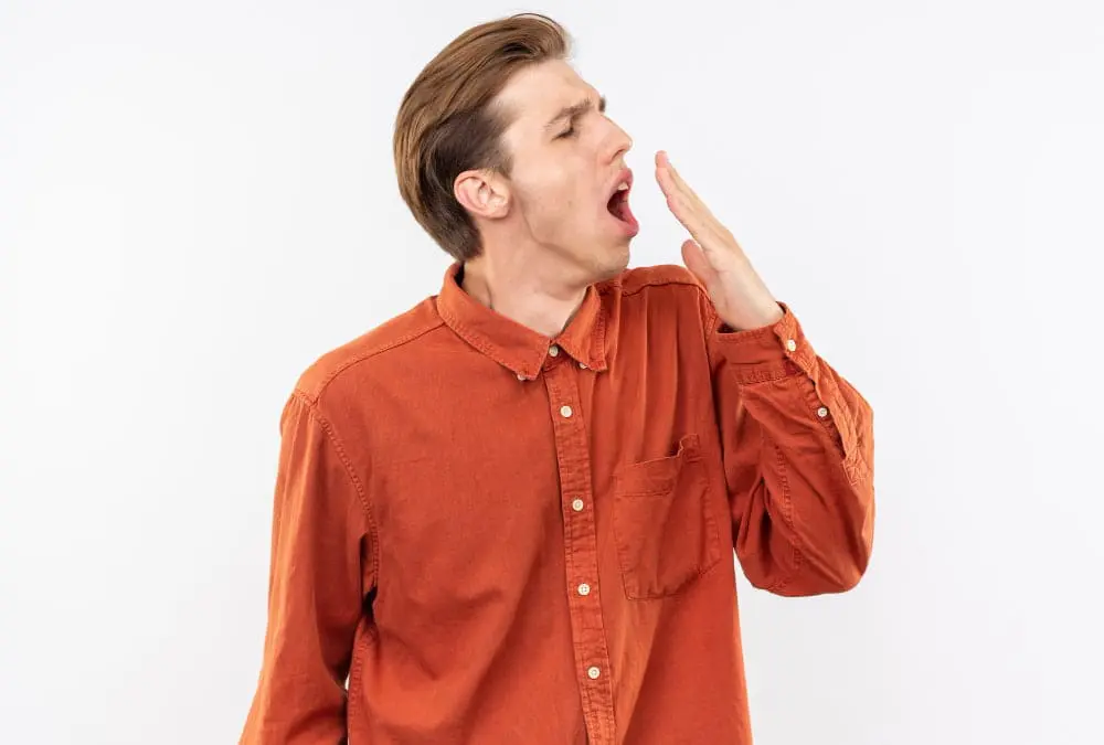 In Jacksonville FL, a person in an orange shirt yawns with one hand covering their mouth, momentarily exposing an underbite against a plain white background.