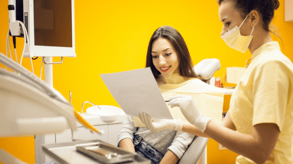 A dental professional in a mask shows a patient a document about orthodontic insurance plans while they sit together in a brightly lit dental office with yellow walls in Jacksonville, FL.