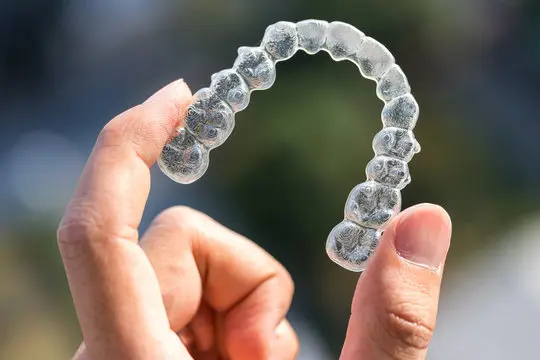 A hand holds a clear dental aligner, used for orthodontic teeth straightening, possibly part of an Invisalign treatment plan in Jacksonville, FL.
