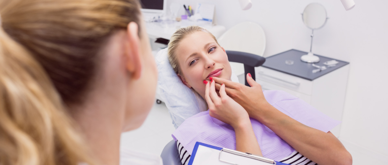 A woman sits in a dental chair touching her lips, looking at a dental professional who holds a clipboard and discusses adult orthodontics in a clinic setting in Jacksonville, FL.