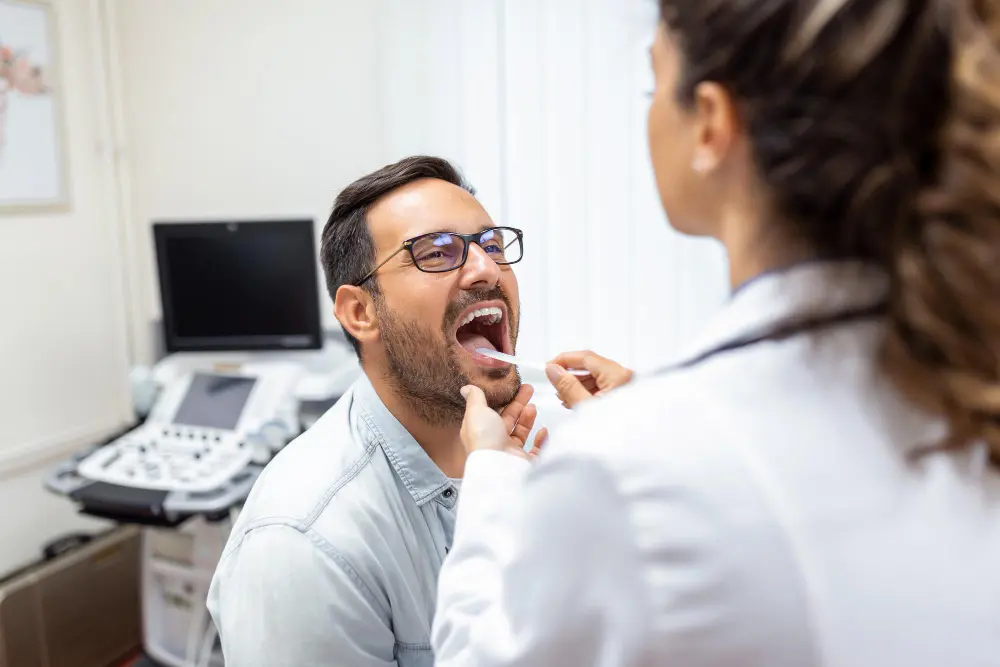 A doctor examines a patient’s throat with a tongue depressor in a medical office, checking for signs of tongue thrust in Jacksonville, FL.