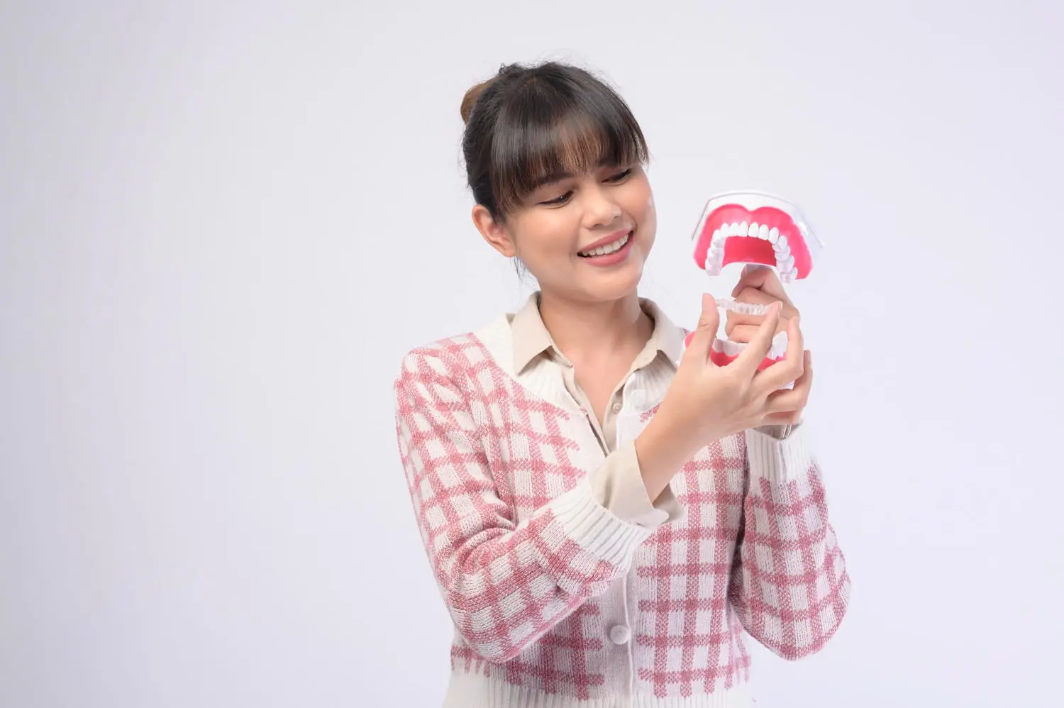 A woman in a pink checkered sweater holds and looks at a dental model with teeth, likely exploring Invisalign treatment options in Jacksonville, FL.