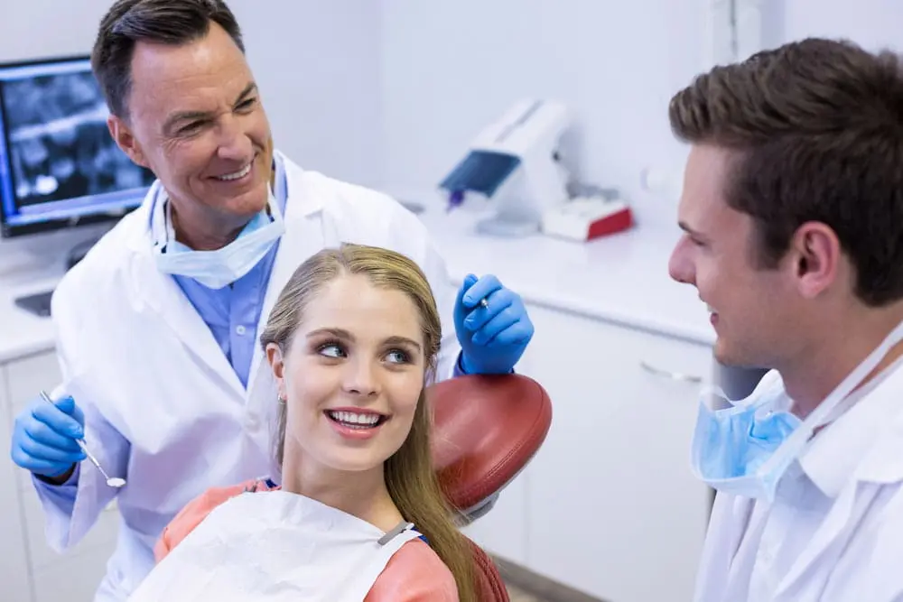 A dentist and a dental assistant talk with a smiling female patient with a palatal expander sitting in a dental chair in a modern clinic in Jacksonville, FL.