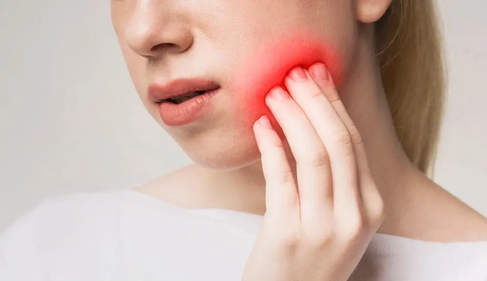 A person holds their jaw with one hand, highlighting a red, irritated area on the side of their face, possibly indicating tooth or jaw pain in Jacksonville, FL, raising questions about treatment options, including Invisalign vs braces.