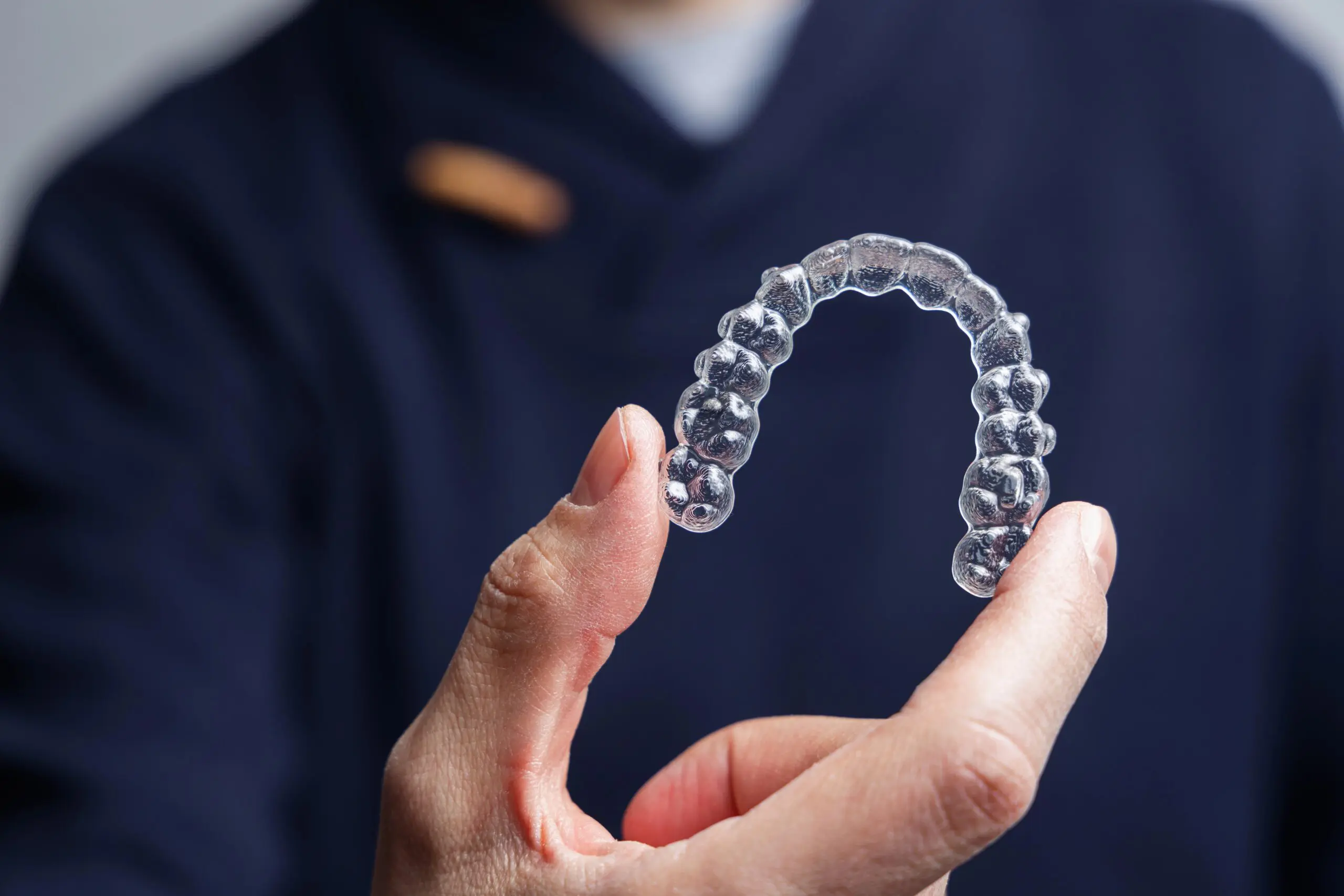 A person holding a clear aligner dental tray between their fingers, with a dark blurred background—perfect for illustrating options like the Invisalign Payment Plan in Jacksonville FL.