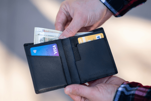 A person holds an open black wallet containing U.S. dollar bills and two credit cards, one blue and one yellow—perfect for budgeting or managing an Invisalign Payment Plan in Jacksonville FL.