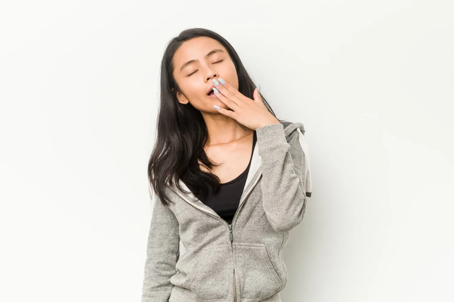 In Jacksonville FL, a woman in a grey hoodie yawns with her hand covering her mouth, a common behavior observed in individuals who are habitual mouth breathers.