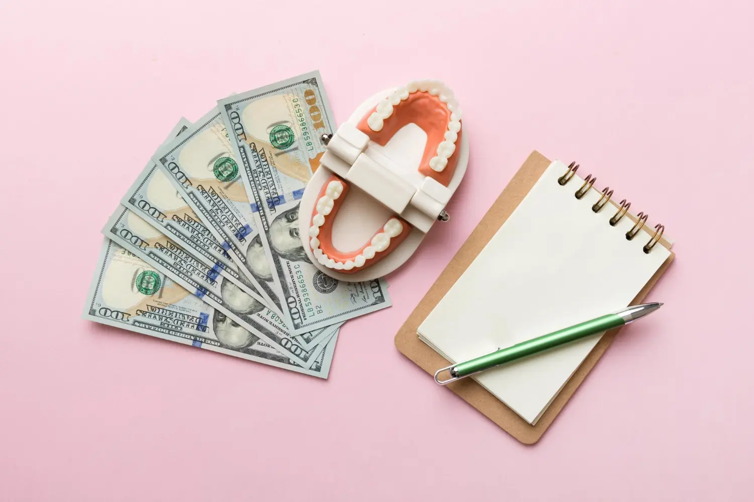 Orthodontic Insurance Plans: A dental model, four $100 bills, a blank notepad, and a green pen are arranged on a pink background in Jacksonville, FL.