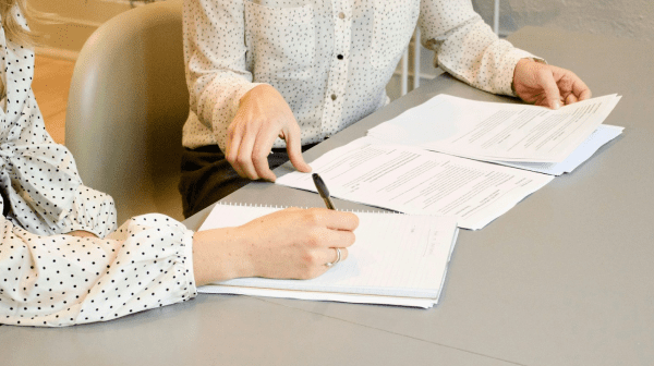 Two people sit at a table reviewing orthodontic insurance plans documents; one is writing in a notebook while the other holds and points at printed papers in Jacksonville, FL.
