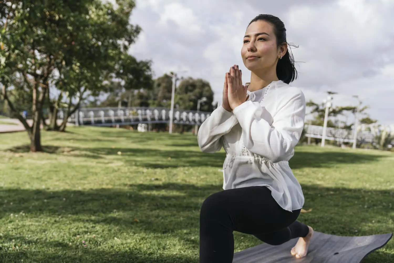 In Jacksonville FL, a woman practices yoga outdoors on a mat, kneeling in a lunge position with hands pressed together—an exercise that can support better posture and breathing habits for mouth breathers