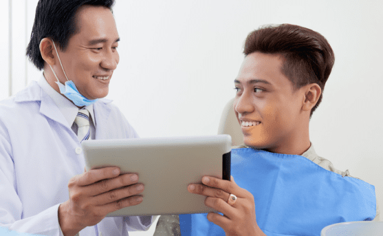 A dentist shows a tablet to a smiling patient sitting in a dental chair, both reviewing information that may relate to jaw surgery options in Jacksonville, FL.