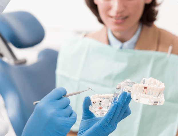 A dentist wearing blue gloves explains a dental procedure to a patient using a tooth model and dental tool, possibly discussing aspects of jaw surgery in Jacksonville, FL.