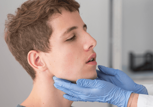 A doctor wearing blue gloves examines a young person's jaw and neck in a clinical setting, possibly assessing recovery following jaw surgery in Jacksonville, FL.