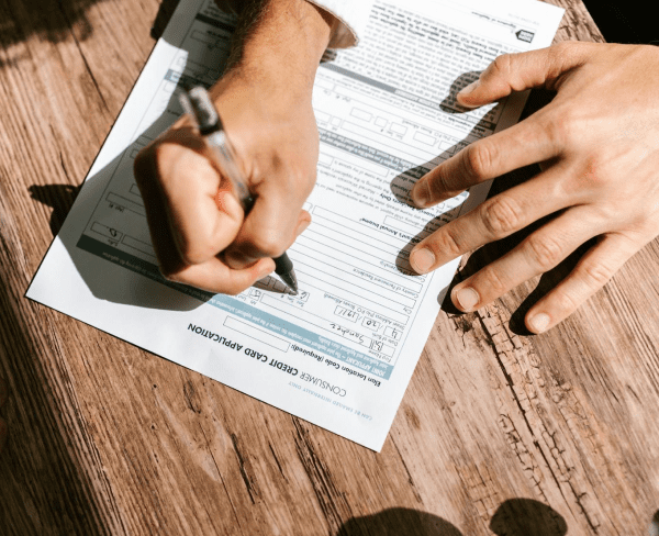 A person fills out a consumer credit card application form with a pen on a wooden surface, possibly preparing for Invisalign insurance coverage in Jacksonville, FL.