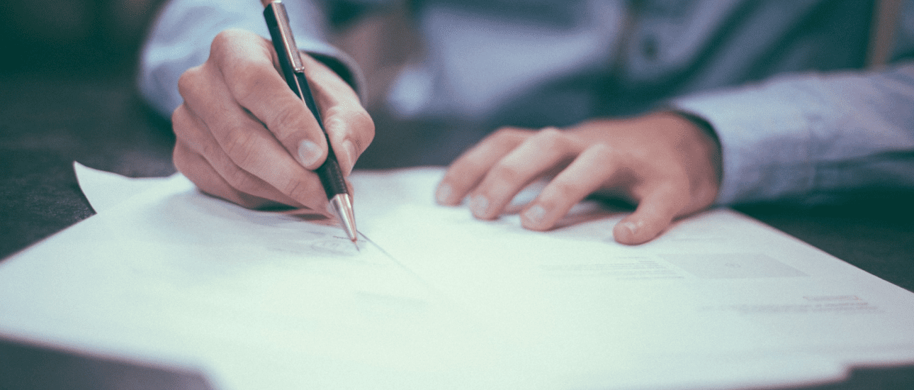 A person wearing a blue shirt writes about orthodontic insurance plans on a white sheet of paper with a black pen at a desk in Jacksonville, FL.
