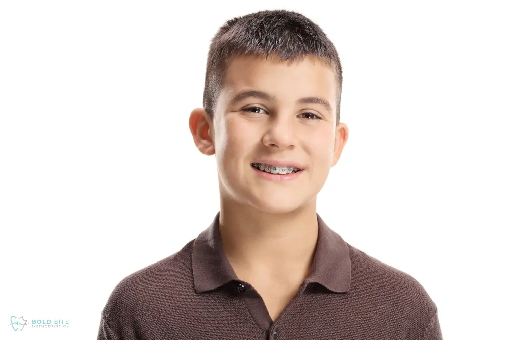 A boy with short dark hair, wearing a brown polo and braces, stands against a white background at Bold Bite Orthodontics' braces for overbite in Jacksonville, FL.