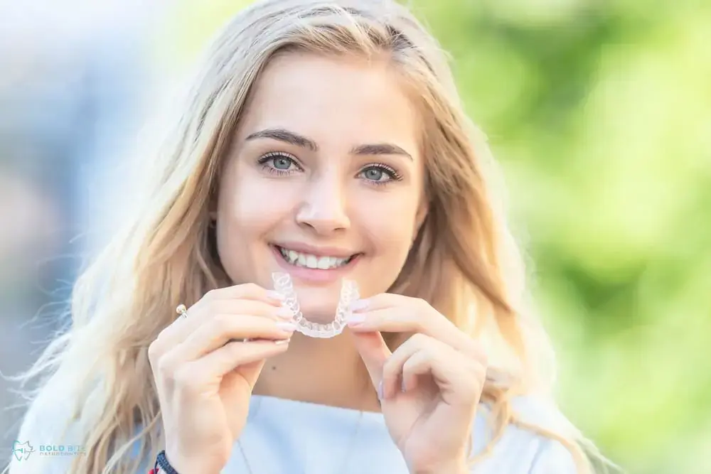 Smiling young woman holding a clear dental aligner outdoors for Bold Bite Orthodontics in Jacksonville, FL - Can Invisalign Fix Overbite in Jacksonville, FL. Smiling young woman holding a clear dental aligner outdoors for Bold Bite Orthodontics in Jacksonville, FL - Can Invisalign Fix Overbite in Jacksonville, FL.
