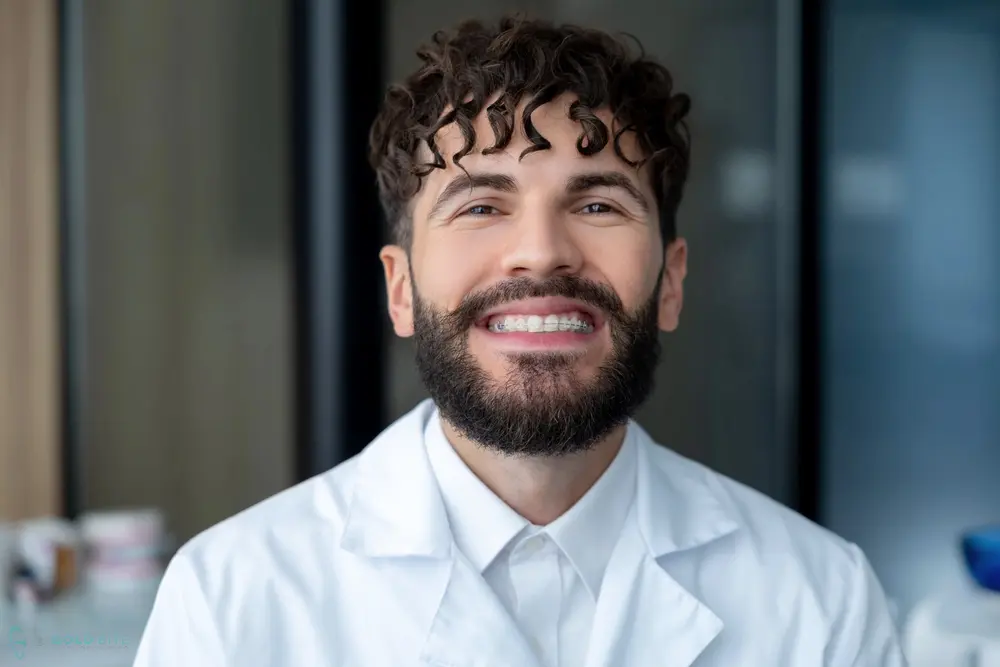 Smiling man with curly hair and beard in a white lab coat at Bold Bite Orthodontics, located in Jacksonville, FL - Clear Braces vs Metal Braces in Jacksonville, FL