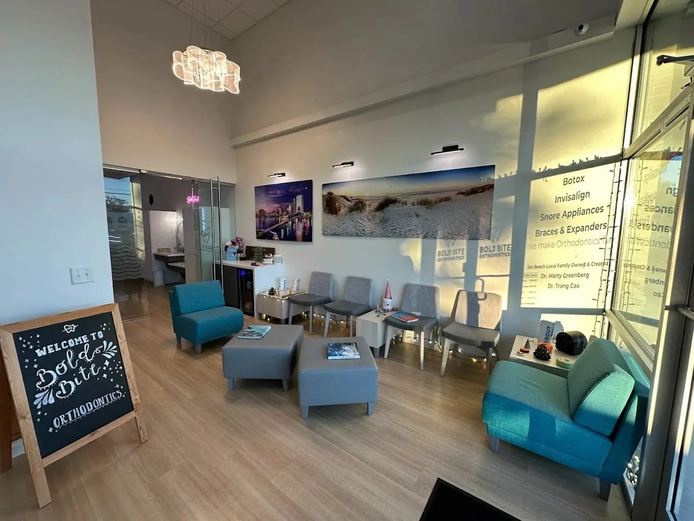 Waiting area at Bold Bite Orthodontics in Jacksonville, FL with teal chairs, chalkboard sign, magazines, art, and large windows.