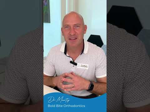 A person wearing a white shirt with a name tag sits at a desk in an orthodontics office. Text at the bottom reads, "Dr. Martz, Bold Bite Orthodontics.