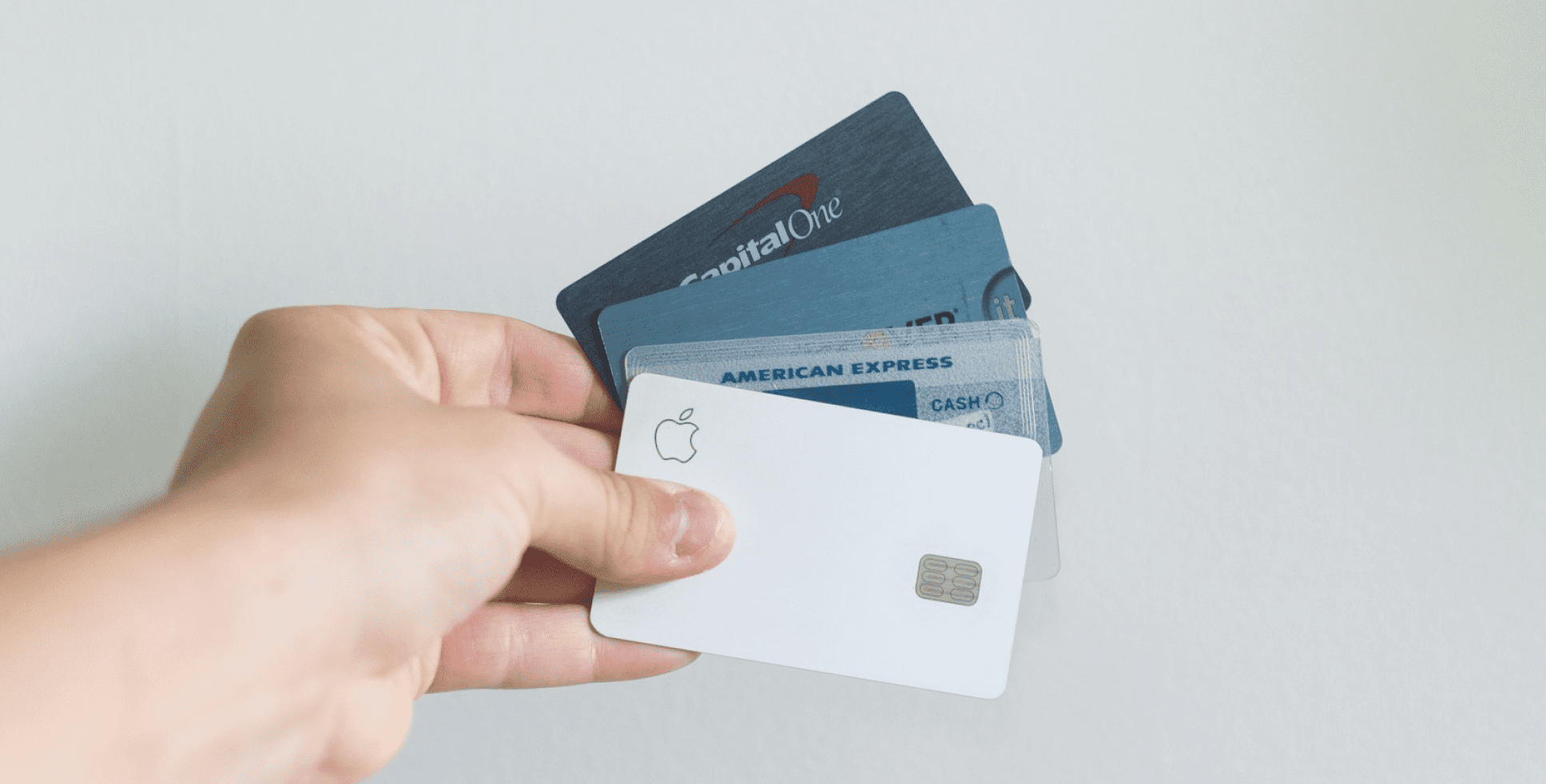 A hand holding several credit cards, including an Apple Card, American Express, and Capital One, against a plain white background in Jacksonville, FL. If you're exploring financing options for dental treatments or other services, contact us to learn about flexible payment plans available in Jacksonville!